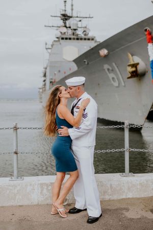 Romantic moment between couple in front of a naval warship at port.