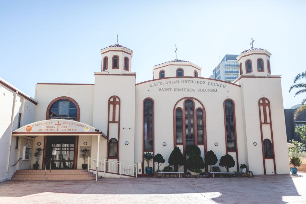 Orthodox church exterior with white walls, three domed towers and arched windows under blue sky.