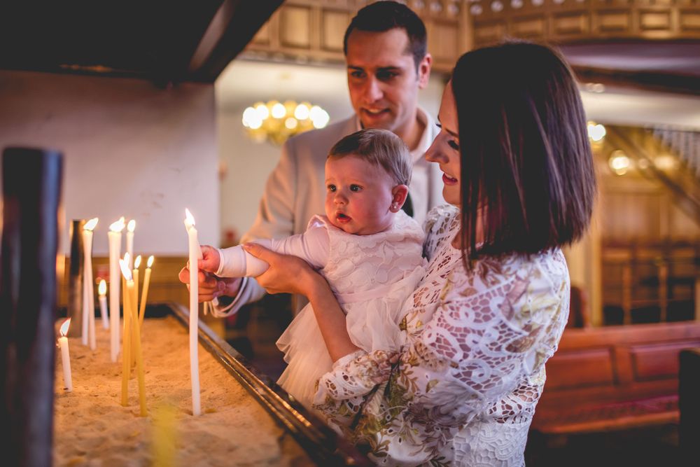 Family lighting candles together during religious ceremony in ornate church interior.