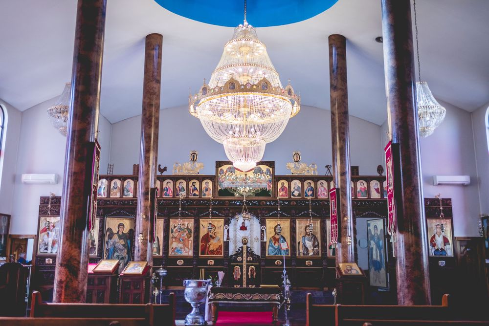 Ornate crystal chandelier hanging in church interior with traditional iconostasis and religious artwork.