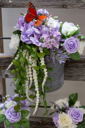 Purple and white floral arrangement with monarch butterfly in rustic metal container.