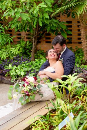 Couple laughing together surrounded by lush tropical plants in garden setting.