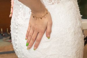 Close-up of bride's hand showing delicate bracelet and green nail polish against white lace dress.