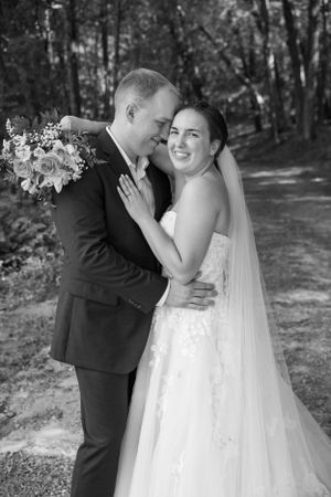 A romantic black and white wedding portrait of a couple embracing on a forest path.