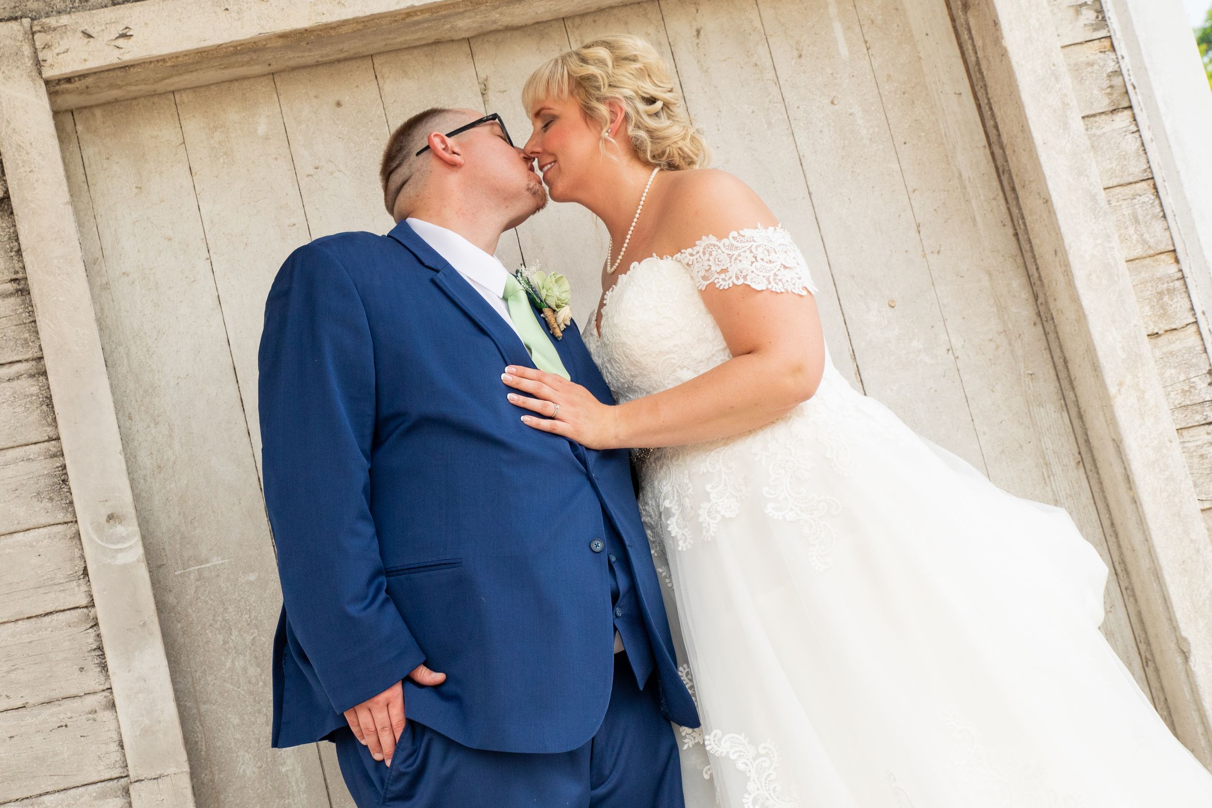 Groom in a navy blue suite, kissing his wife at Old Mill in Marion, MI