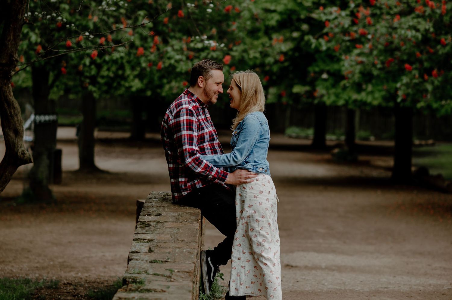 Couple shares an intimate moment while leaning against a stone wall in a garden setting.