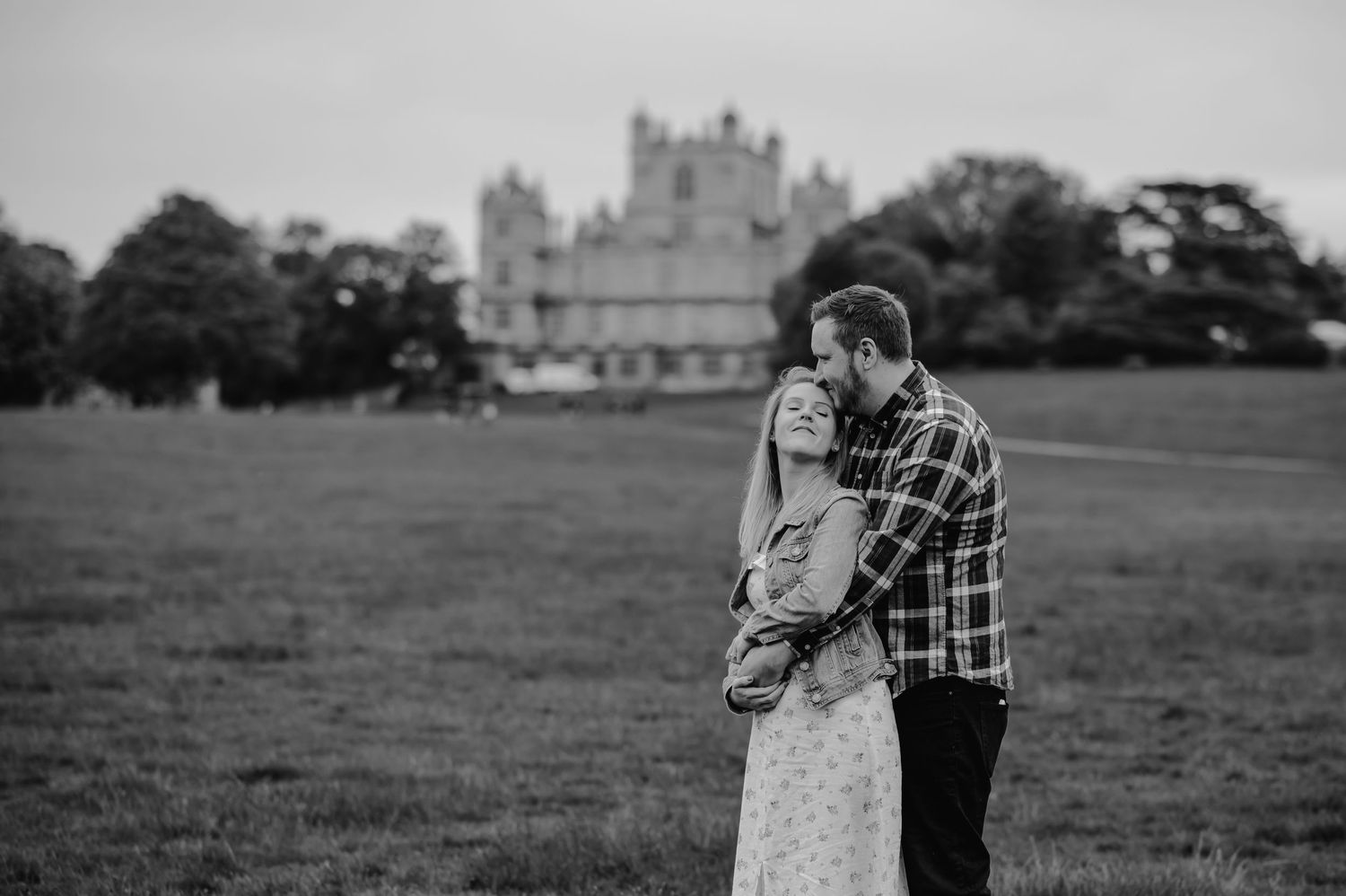Romantic couple embraces in front of a majestic castle on a sprawling lawn in black and white.