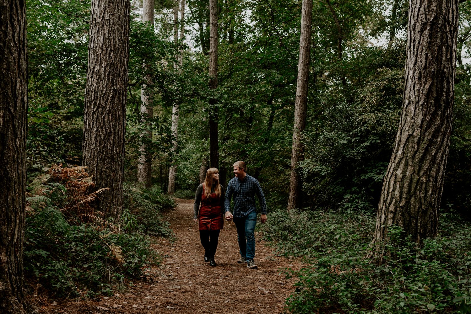 Couple walks hand in hand along wooded trail during forest engagement session.