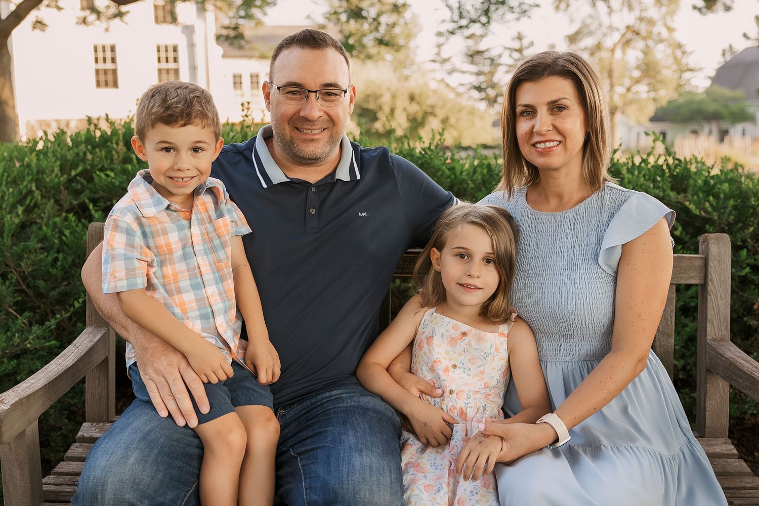 Family of four sitting together on a wooden bench in a garden setting during golden hour.