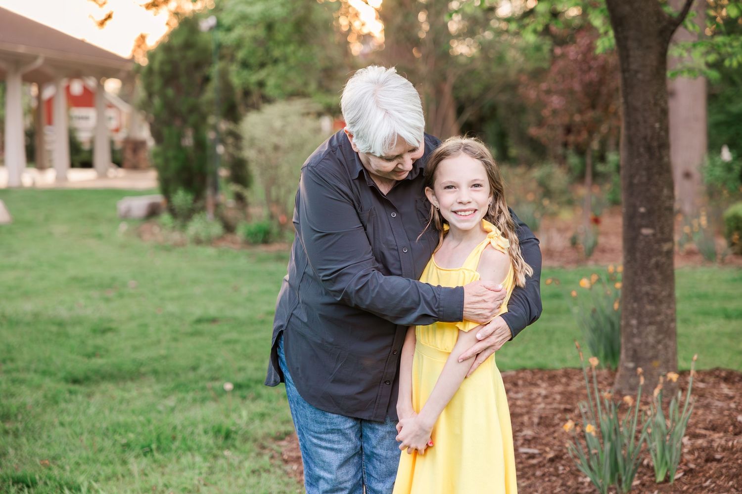 A sweet moment captured between two people standing by a tree in a backyard garden.