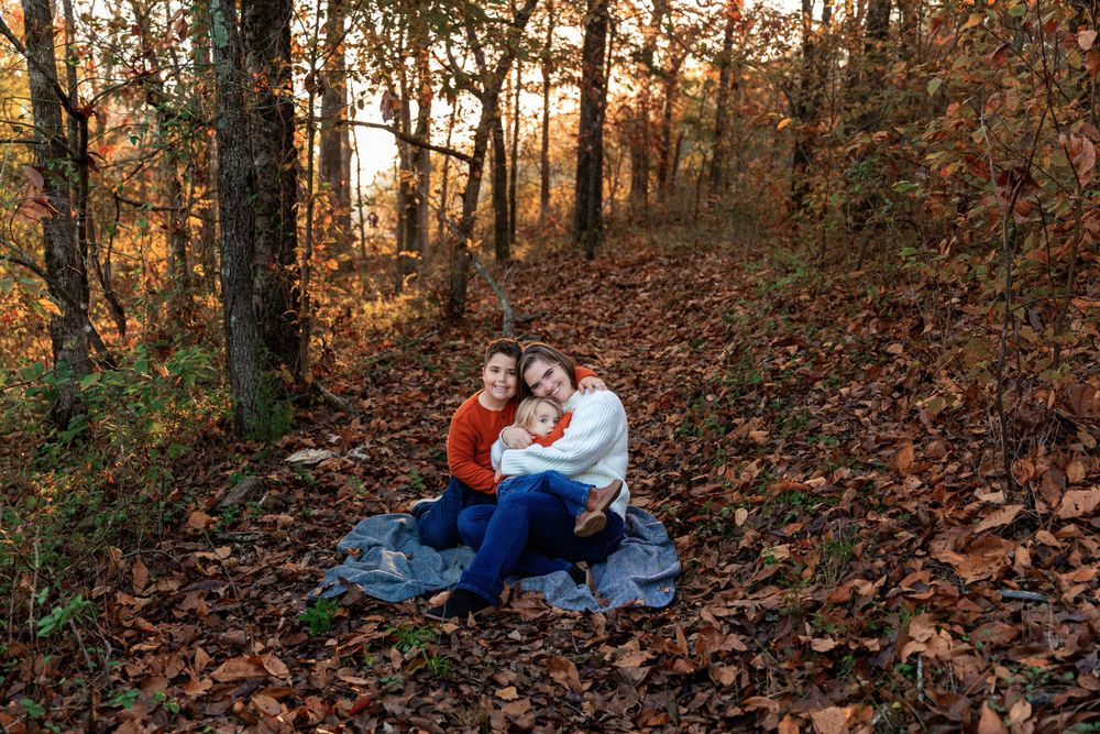 Autumn family photography session in a wooded area with fallen leaves.