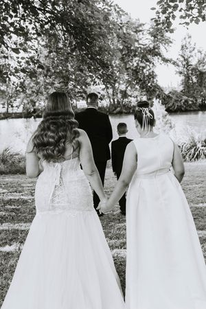 Wedding party in white dresses and formal attire standing together outdoors in black and white photo.
