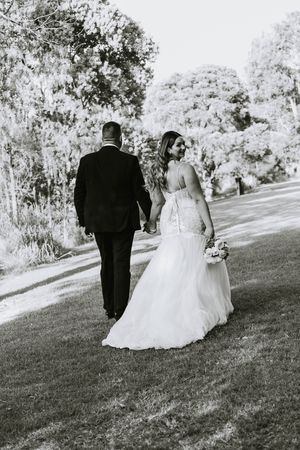Bride and groom walking on grassy hill in black and white wedding photography.