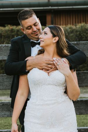 Romantic wedding couple embracing in formal attire outdoors.