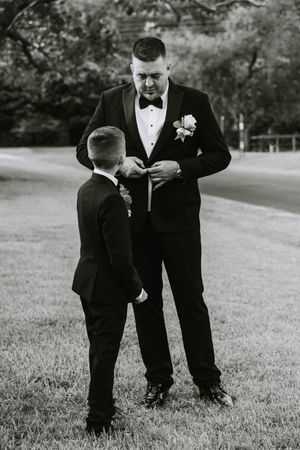 Wedding party members in formal attire interacting on grassy field.