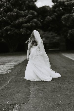 Artistic black and white sequence of a wedding dress trailing along a path.