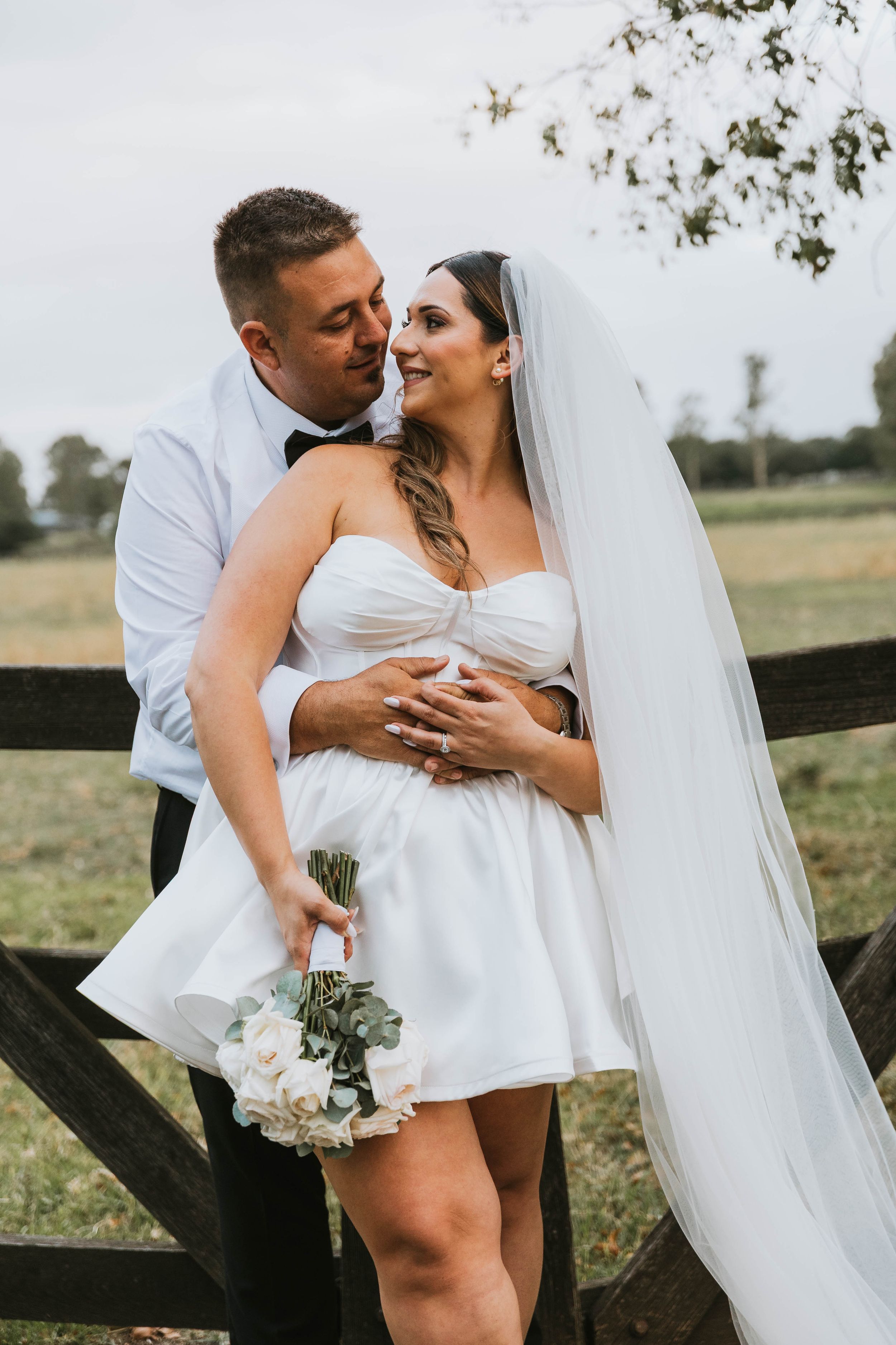 Intimate wedding photos taken against a rustic fence in a countryside setting.