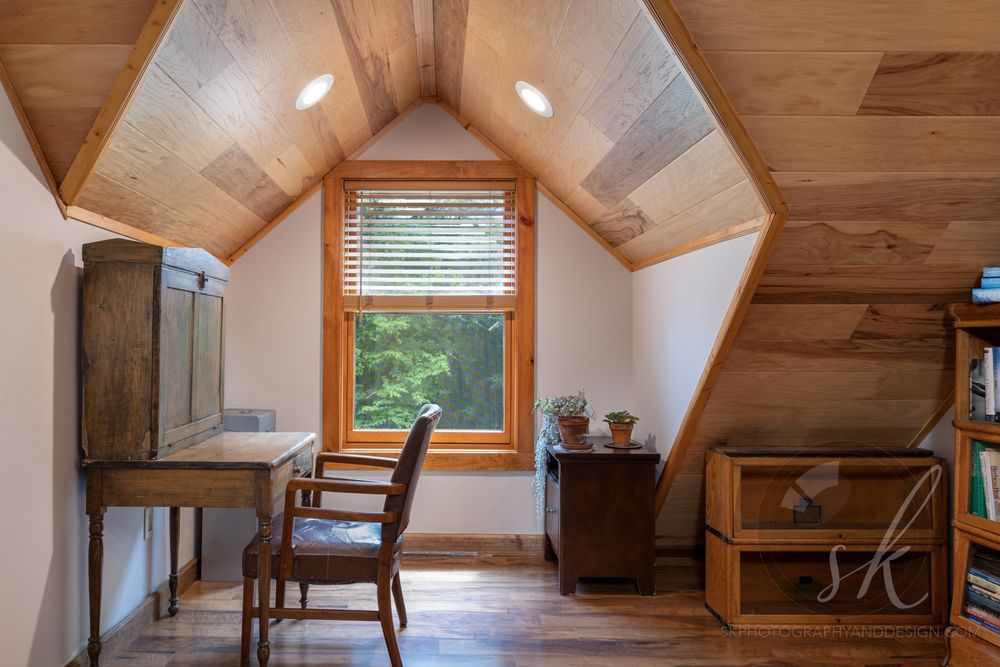 Wooden beams line the vaulted ceiling of a modern loft space with white walls and hardwood flooring in this photo of a home on Schroon Lake.