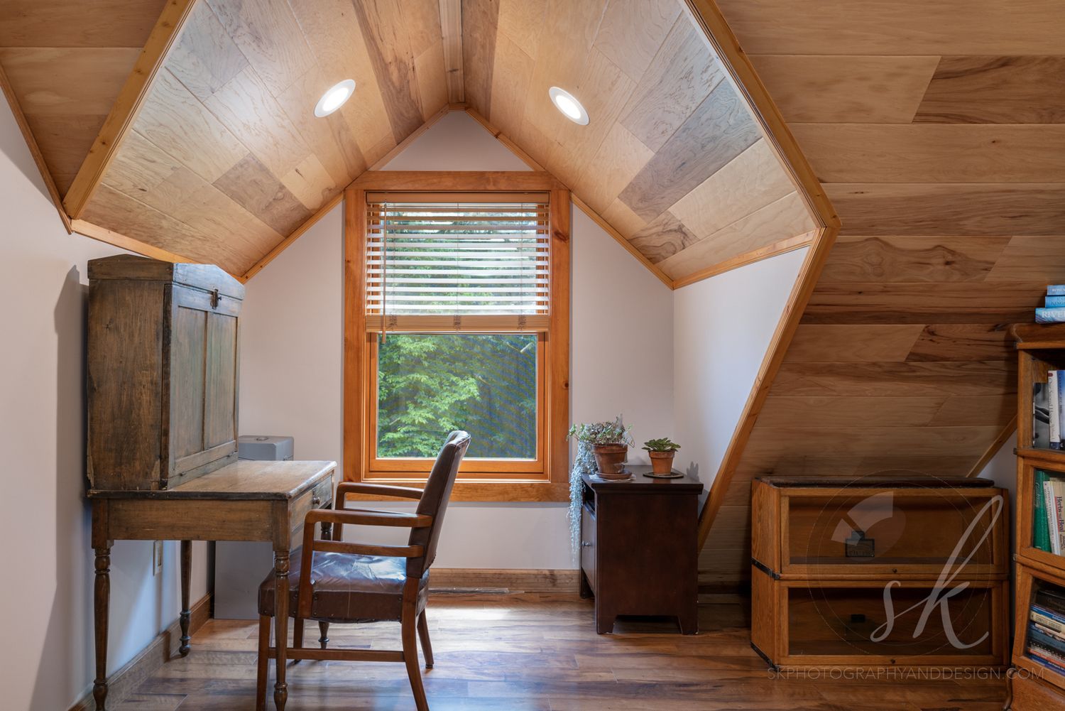 Wooden beams line the vaulted ceiling of a modern loft space with white walls and hardwood flooring in this photo of a home on Schroon Lake.
