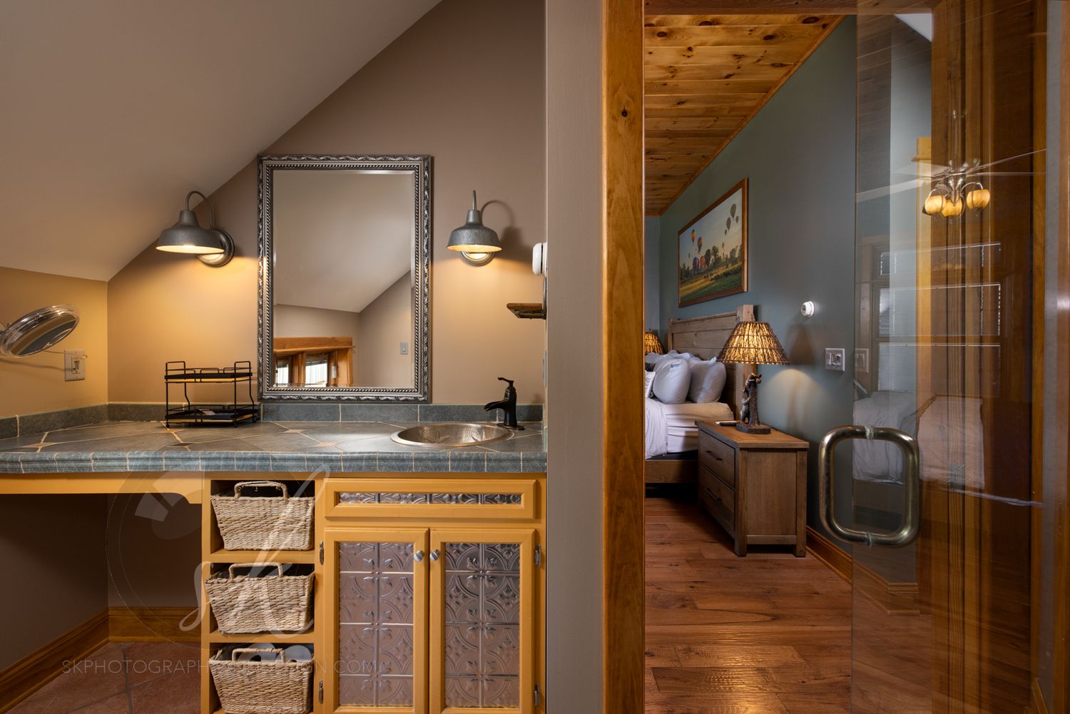 An interior luxury photo of an Adirondack style vacation rental showing a bathroom with primary bedroom beyond.
