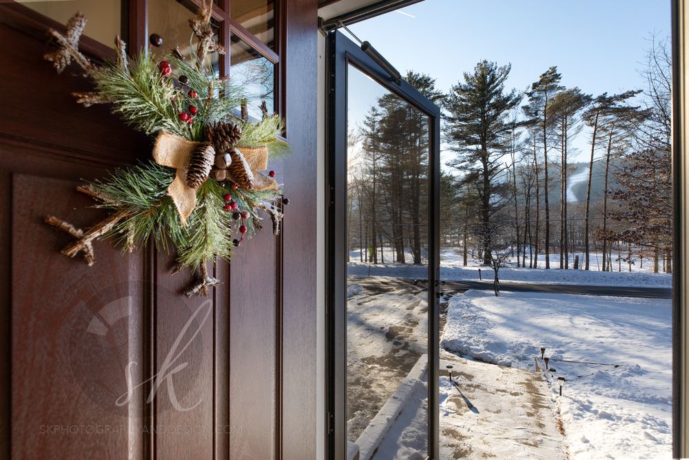 A snowy winter landscape with ski slopes and evergreen trees visible through large glass windows.