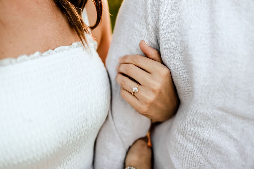 Close-up shot of a couple in white clothing showing an engagement ring.
