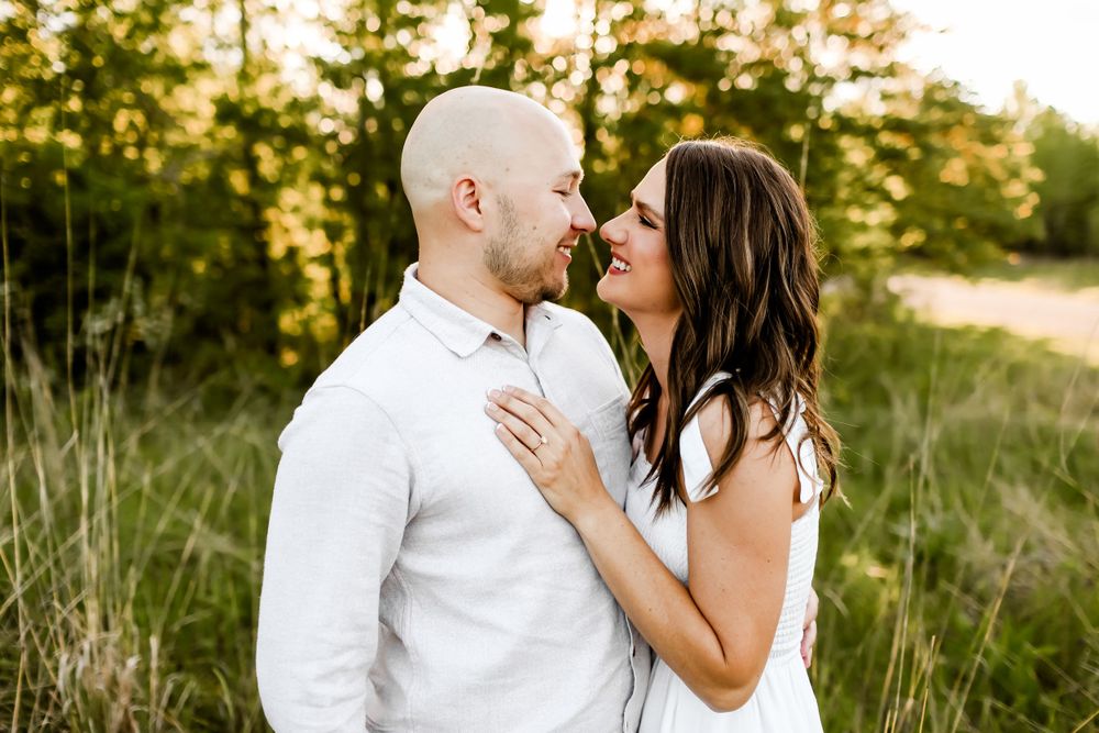 Romantic couple in white outfits sharing an intimate moment at sunset in a grassy field.