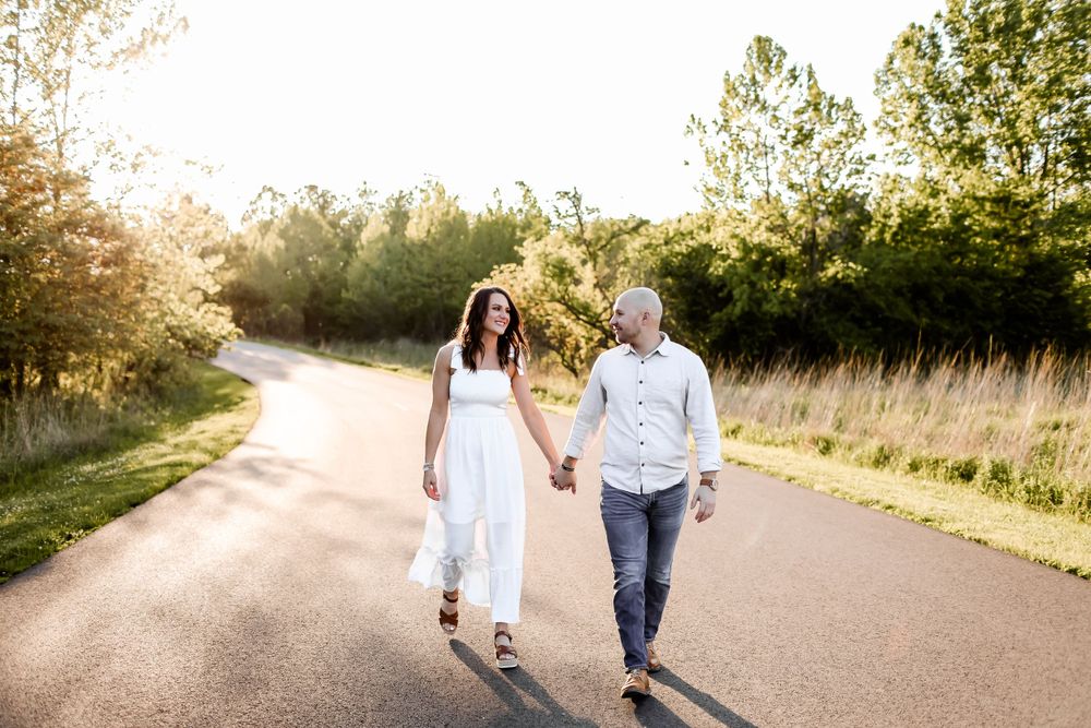 Couple in white clothing walking together on a sunlit country road.