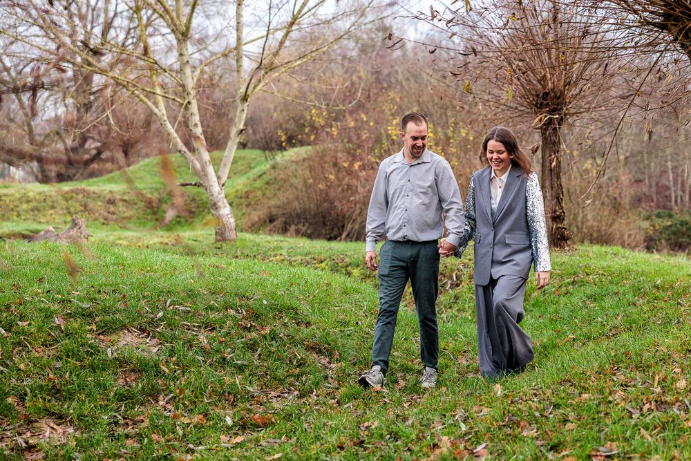 A couple walks together through a wooded area on a fall day during a photo session.