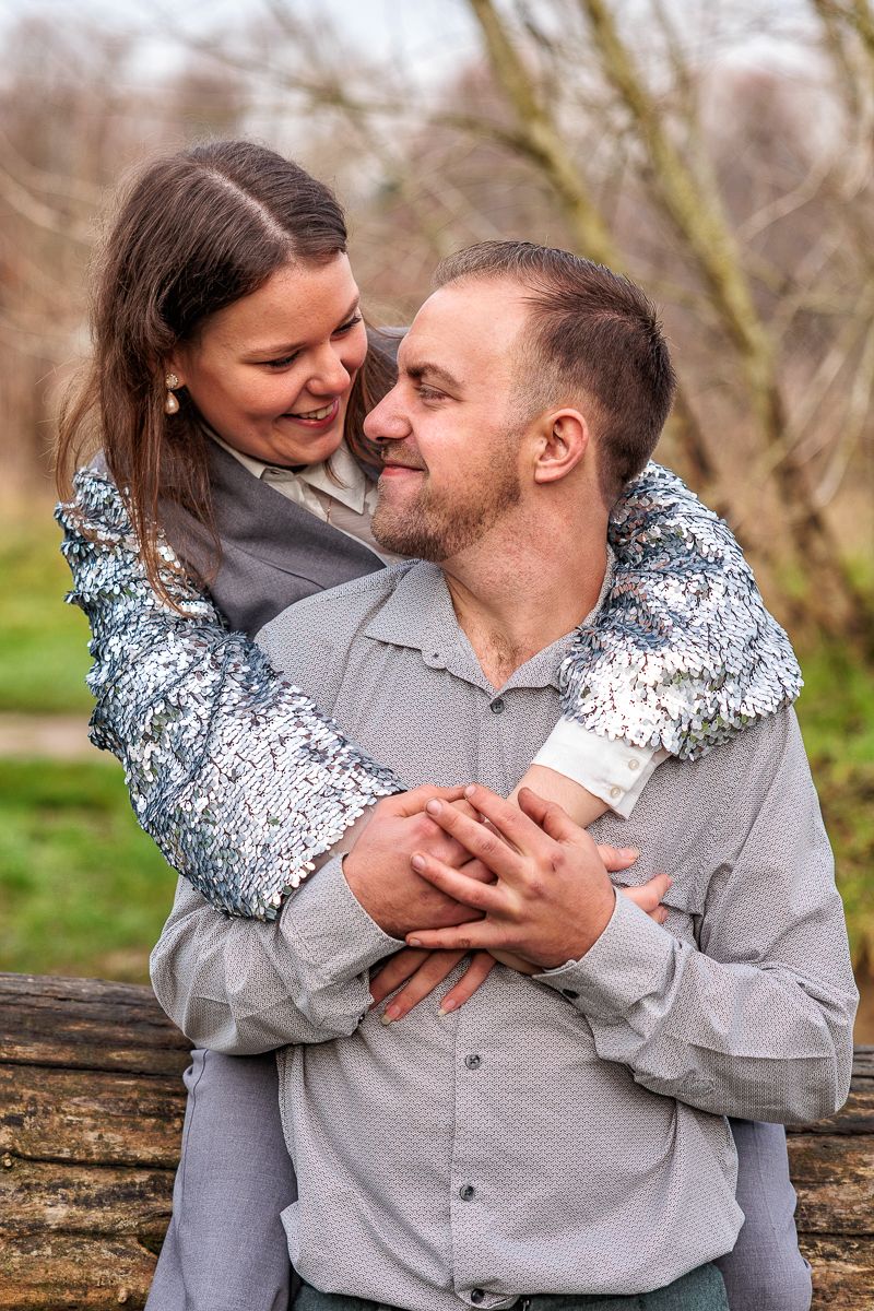 A couple shares intimate moments while sitting on a fallen tree trunk in an outdoor setting during autumn.