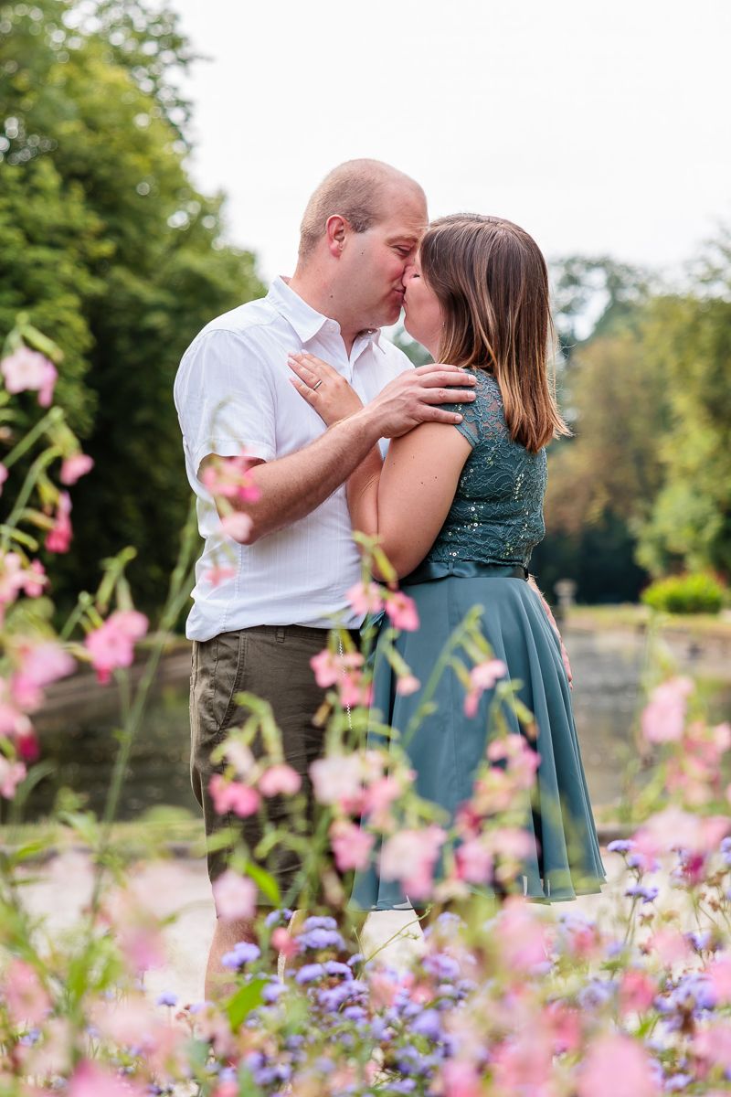 Couple sharing a romantic kiss surrounded by colorful pink and purple wildflowers in a lush garden setting.
