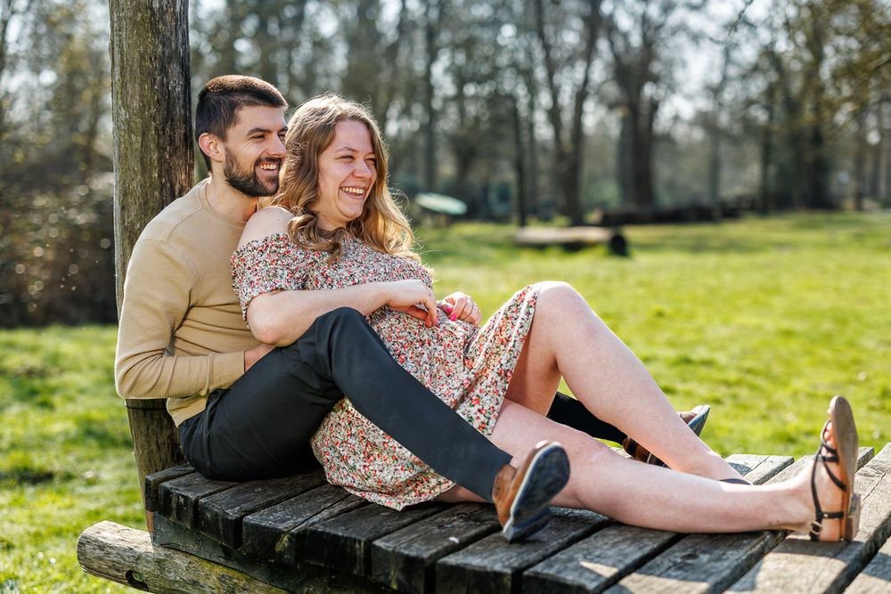 Happy couple sitting on a wooden bench in a sunny park, smiling and relaxing together outdoors.