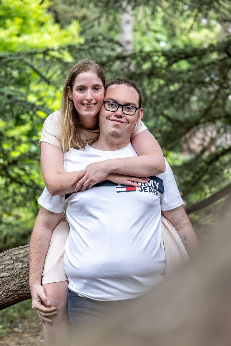 A couple embraces while standing outdoors in a natural forest setting with green foliage in the background.