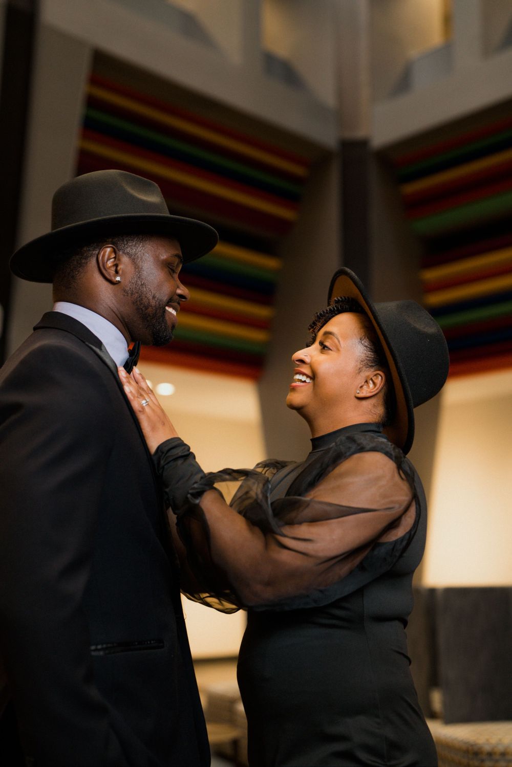 An elegant Black couple in matching black outfits and fedora hats share a joyful moment together in Cincinnati