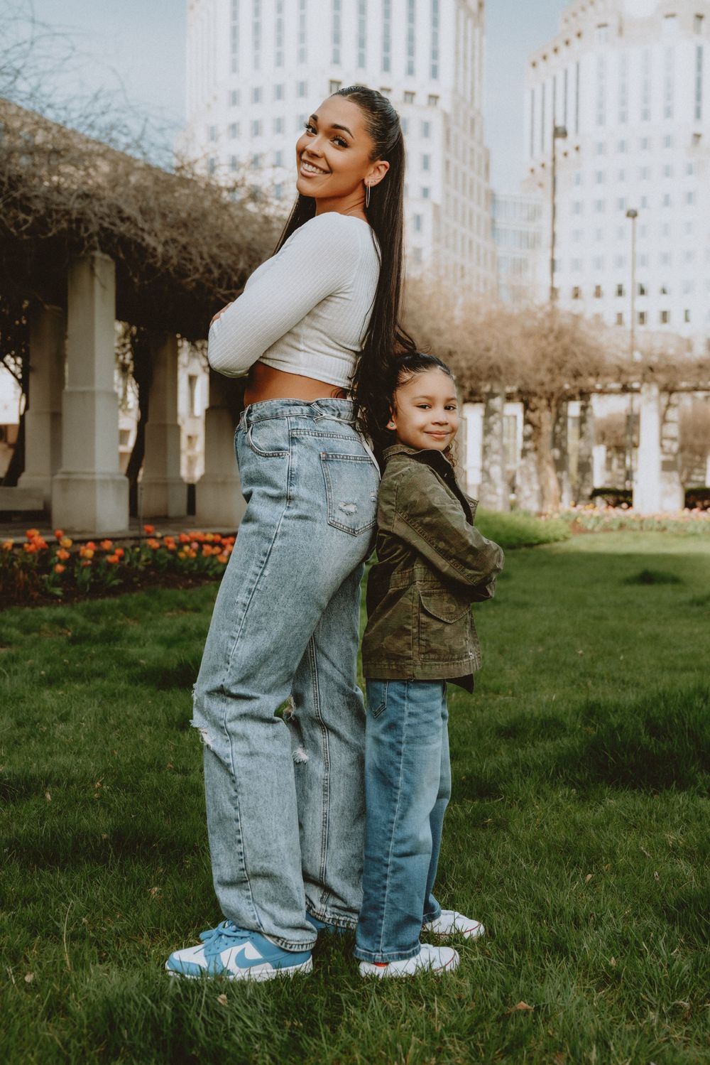 Tall young woman and little girl standing back-to-back smiling in an urban park in Cincinnati
