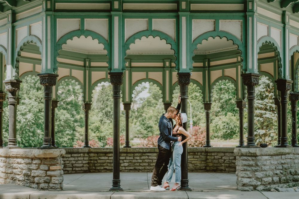 Engagement session with couple sharing a romantic kiss under an ornate green gazebo surrounded by lush greenery in Cincinnati