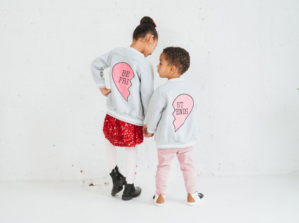 Two children wearing matching best friends heart sweatshirts holding hands against white wall in Cincinnati