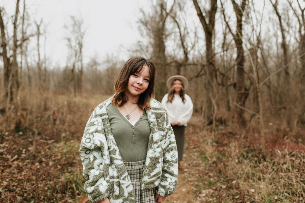 Mother and daughter in floral oversized cardigan and green top posing in bare winter woodland setting in Cincinnati