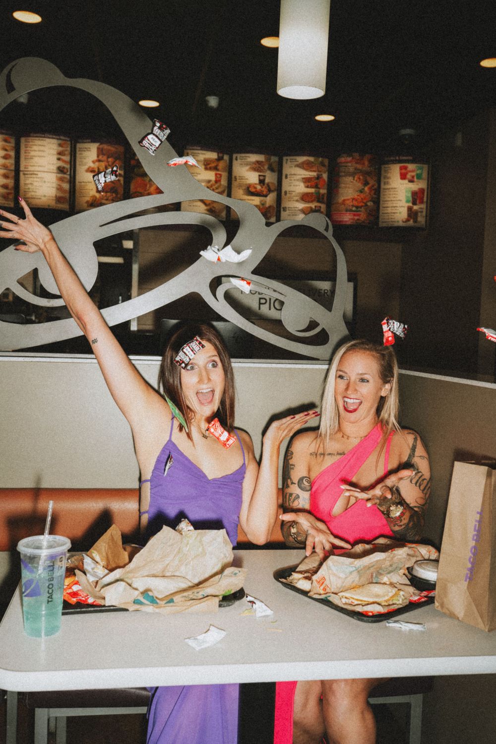 Two women in colorful dresses celebrating their birthday at Taco Bell, throwing sauce packets in the air in Cincinnati