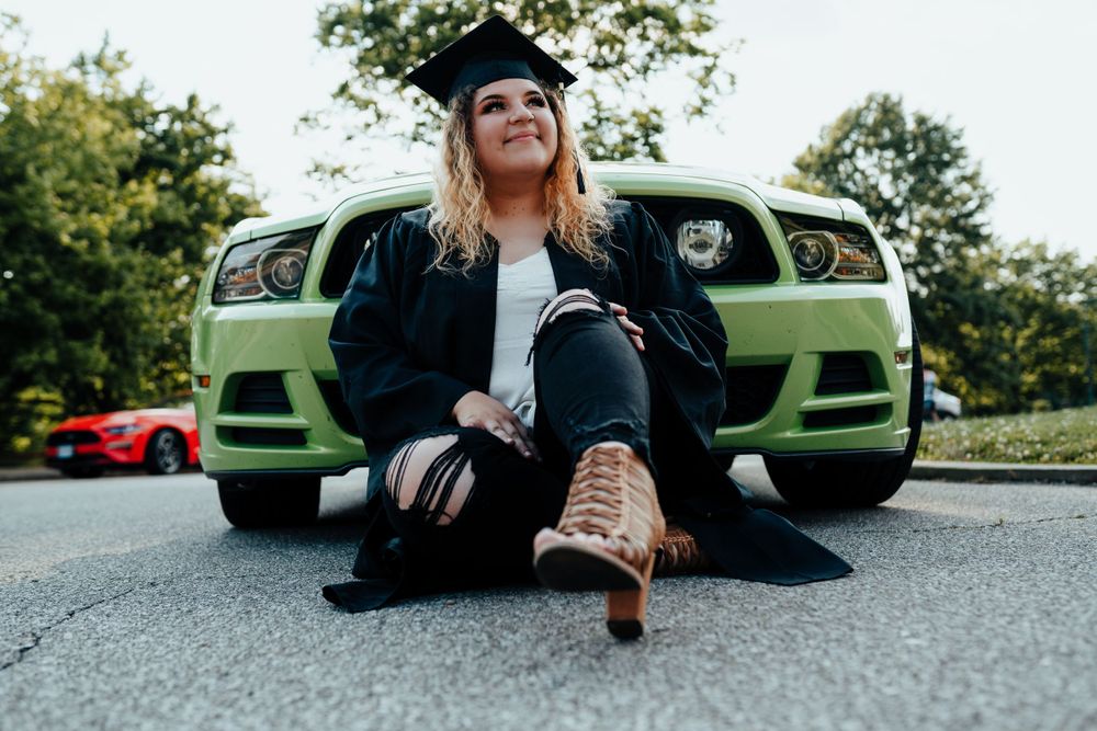 Female graduate in cap and gown sitting in front of green Mustang car for graduation photos for her senior session in Cincinnati