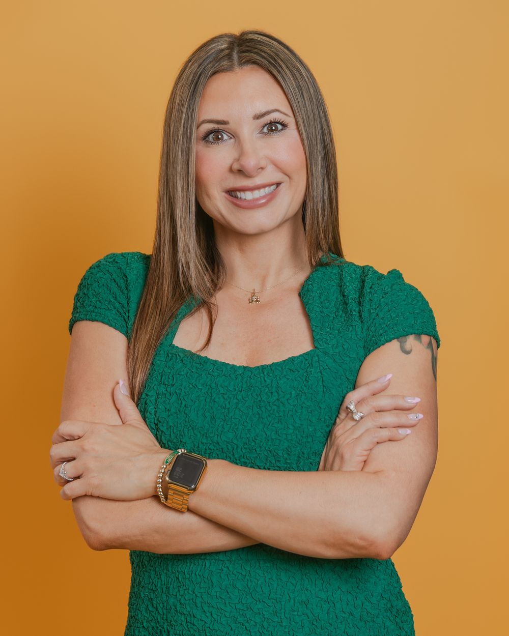Confident person in emerald green top poses with crossed arms against orange background showing different expressions.