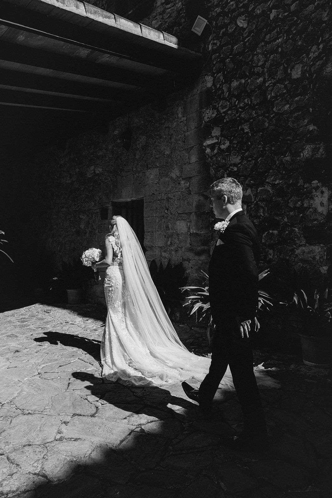 A couple wearing wedding attire walking into the light.