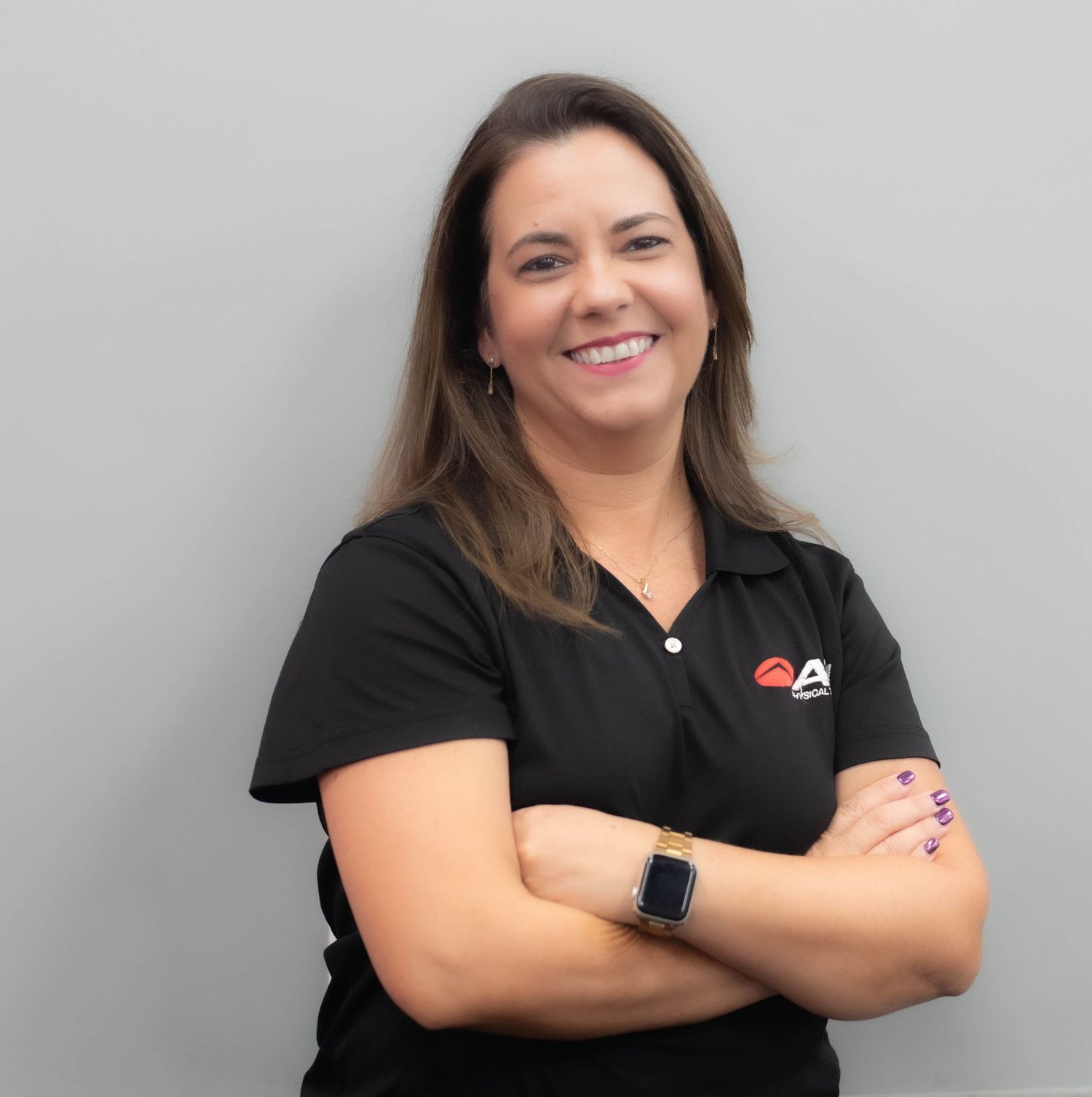 Professional woman in black polo shirt smiling with arms crossed against gray background.