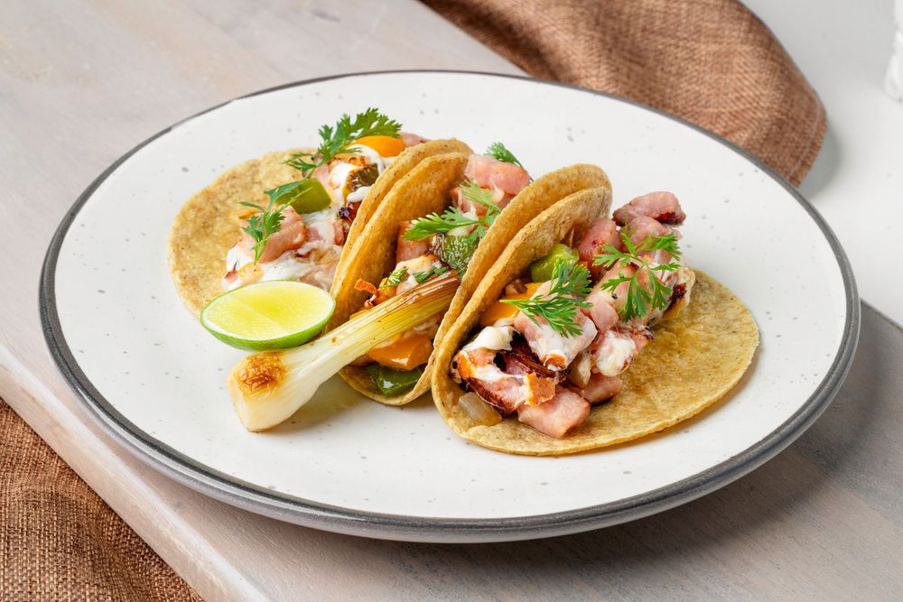 Fresh street tacos garnished with cilantro and lime on white plates.