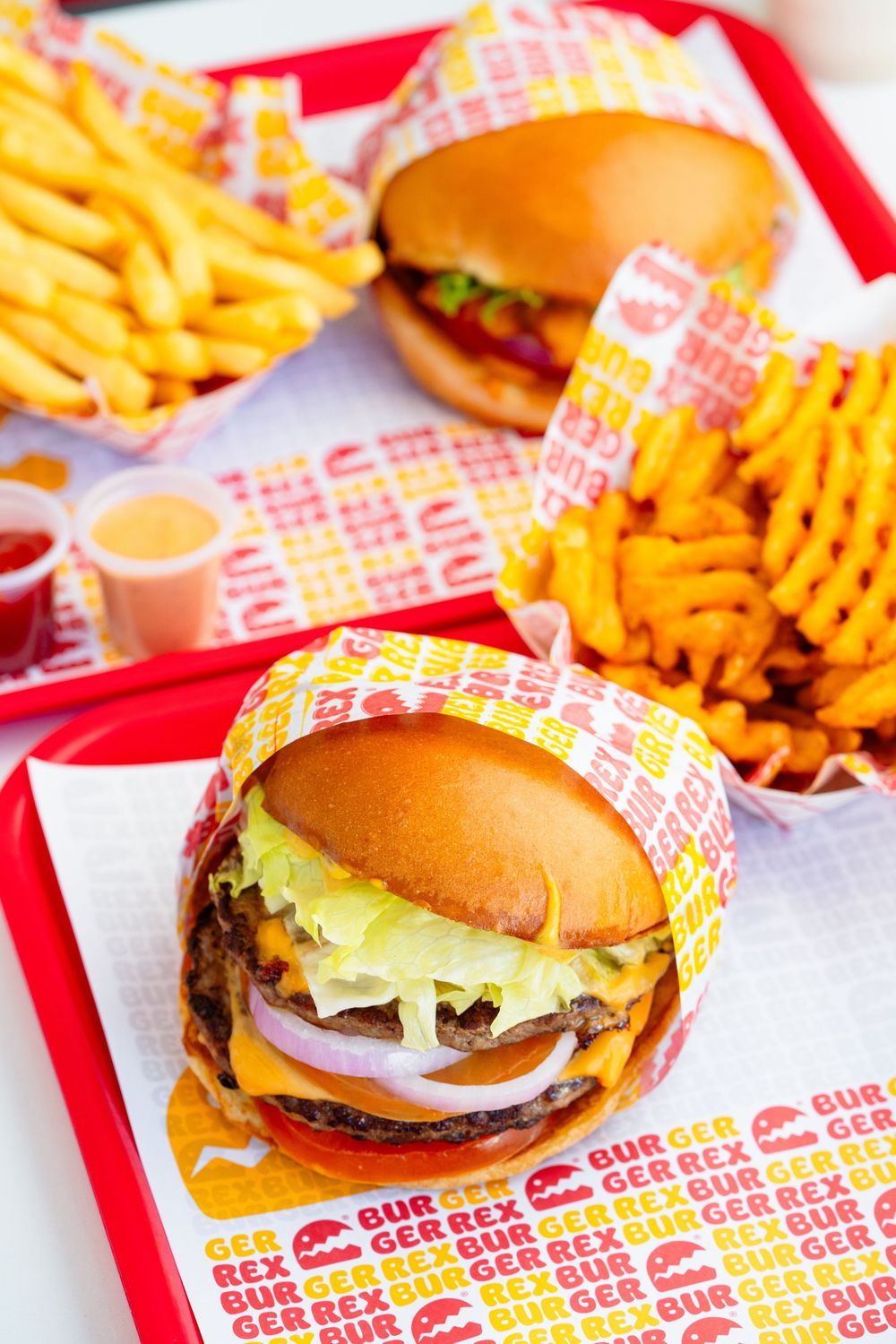 Multiple cheeseburgers with lettuce and tomato on branded red paper wrappers.