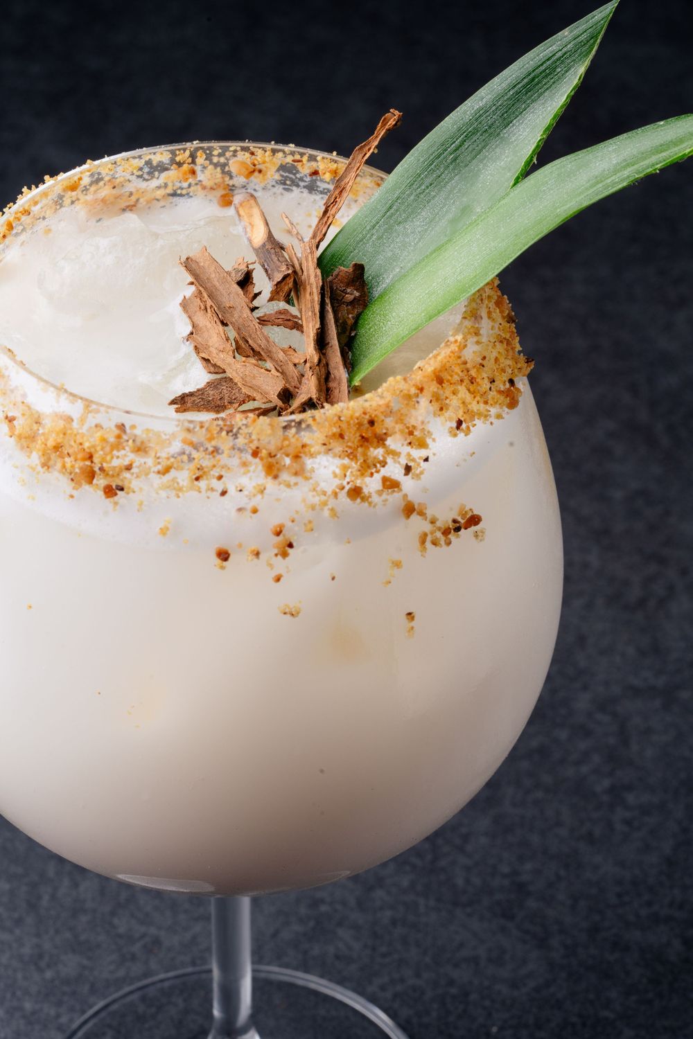 White tropical cocktail with coconut rim garnished with pineapple leaves.