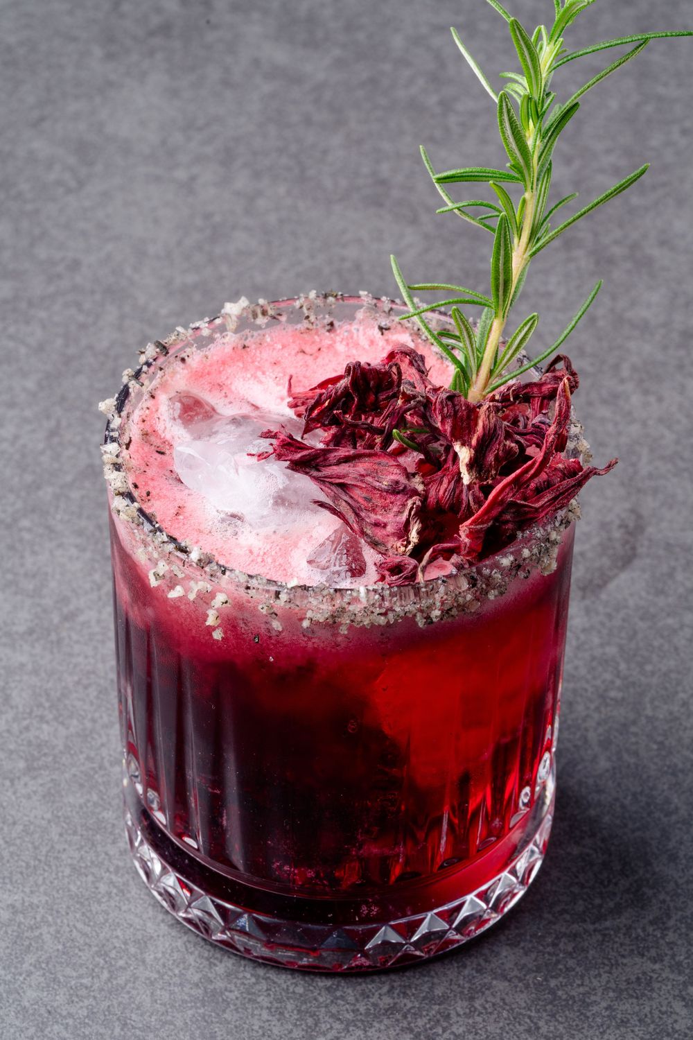 Red cocktail with crushed ice garnished with fresh rosemary in a crystal glass.
