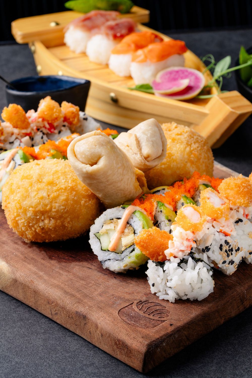 Assorted sushi rolls and tempura served on a wooden board with garnishes.
