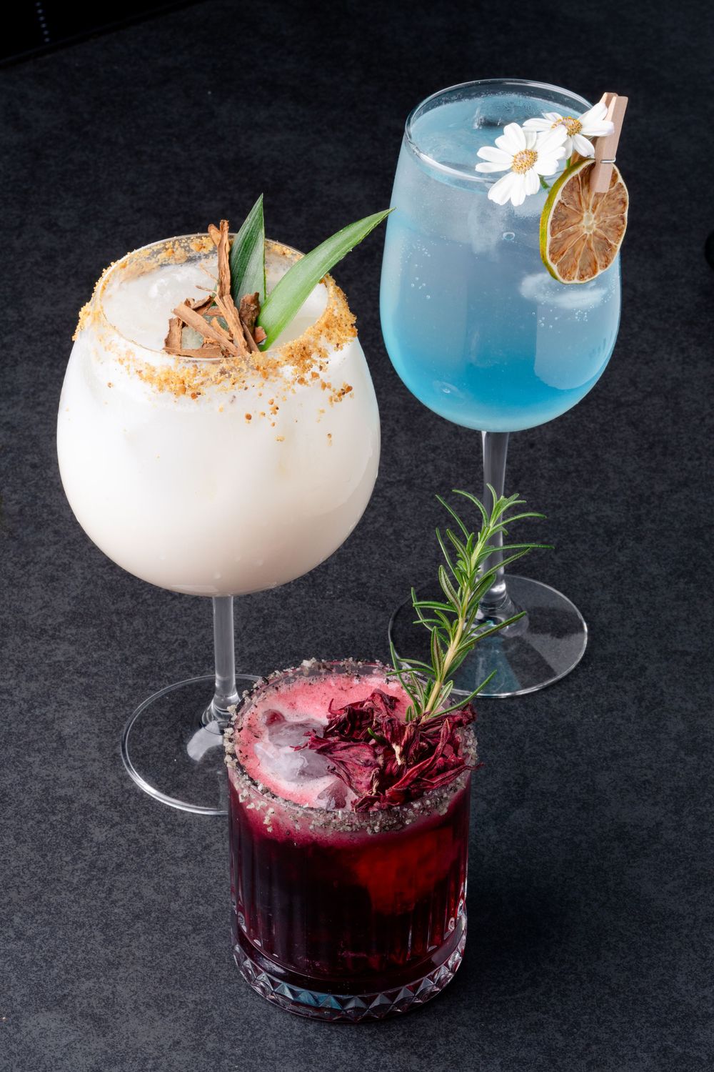 Elegant cocktails in various colors garnished with herbs and fruit.