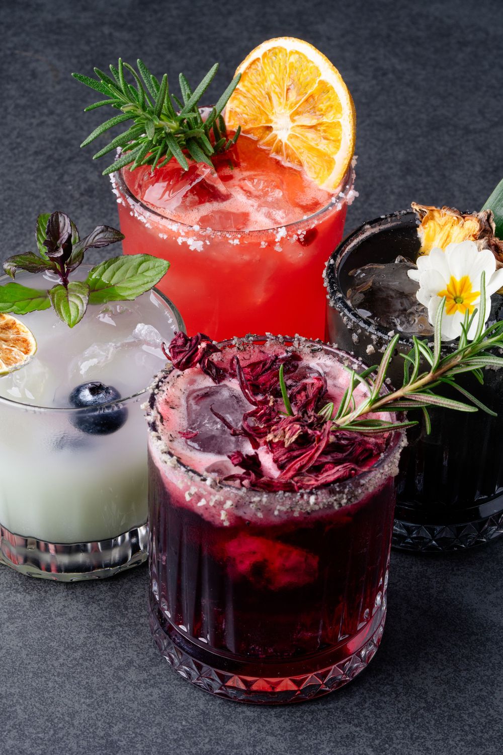 Colorful craft cocktails with fruit and herb garnishes on dark background.